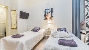 A hotel room with two beds, a TV, a painting, a lamp, and a window with curtains. - Go Happy Home Apartment Mikonkatu 18 (Helsinki)