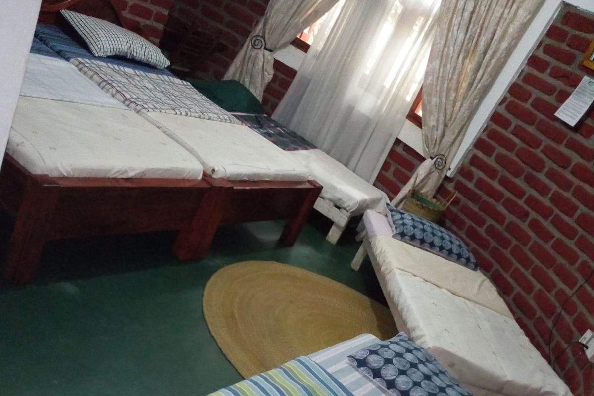 A room with two wooden beds, a woven mat, and brick walls.