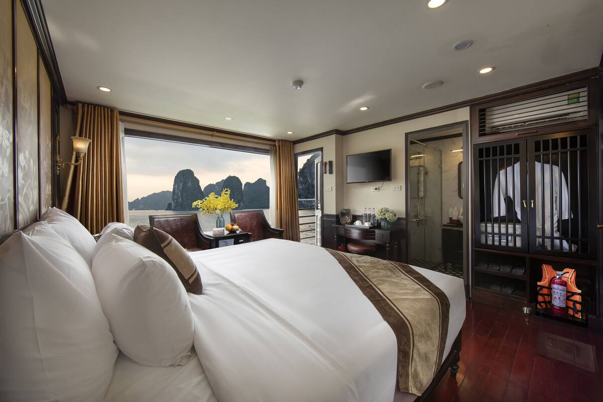 A spacious hotel room with a large bed, a desk with a chair, a TV mounted on the wall, and a view of the mountains through the window.