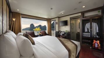 A spacious hotel room with a large bed, a desk with a chair, a TV mounted on the wall, and a view of the mountains through the window.