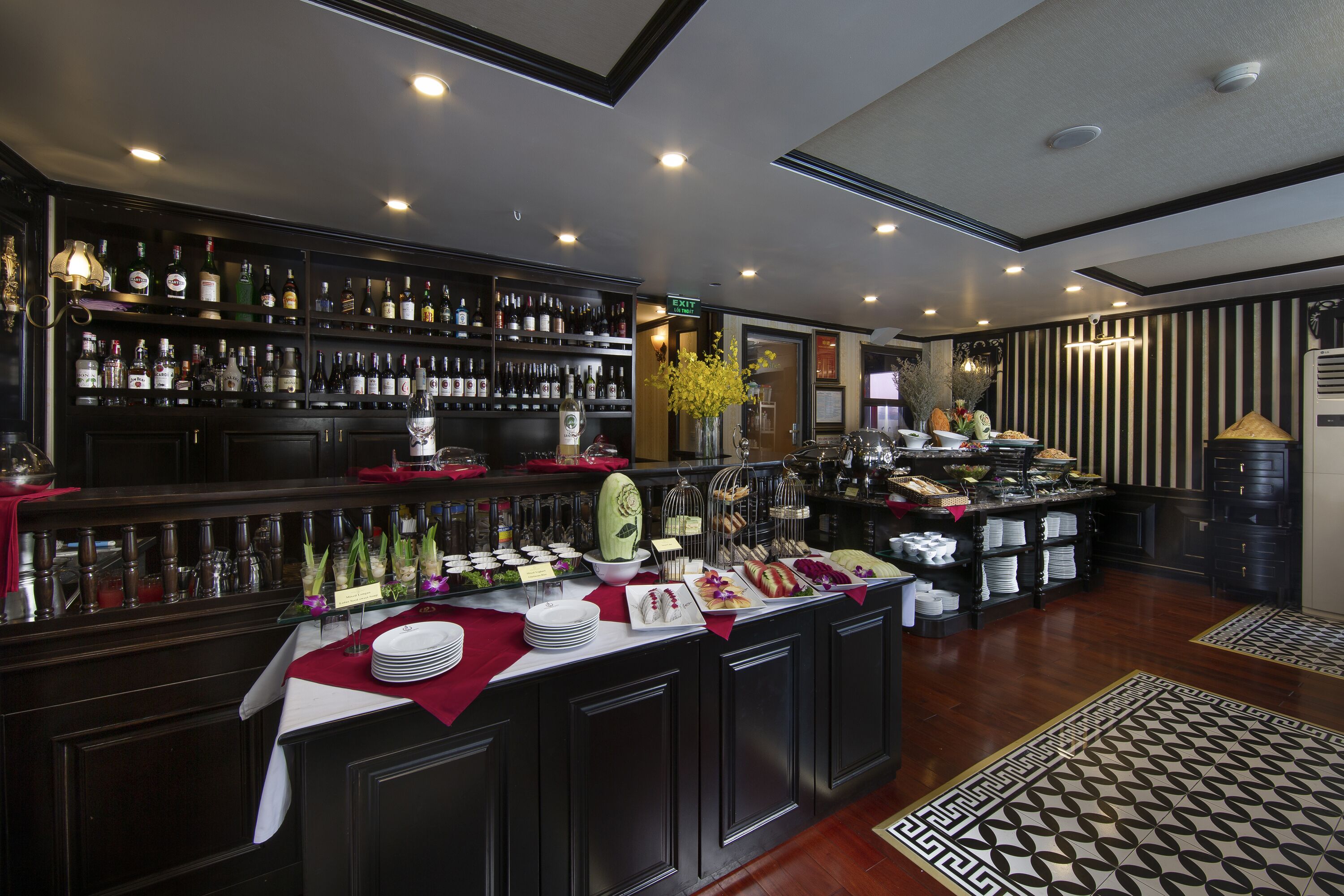 A bar area with shelves of liquor bottles, a buffet with various dishes, and a patterned floor.