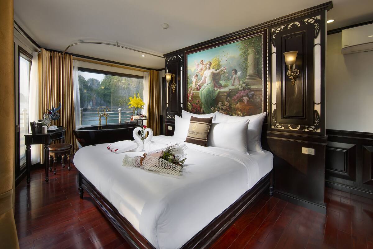 A large, elegantly furnished bedroom with a large bed, a desk, and a view of a body of water through a window.