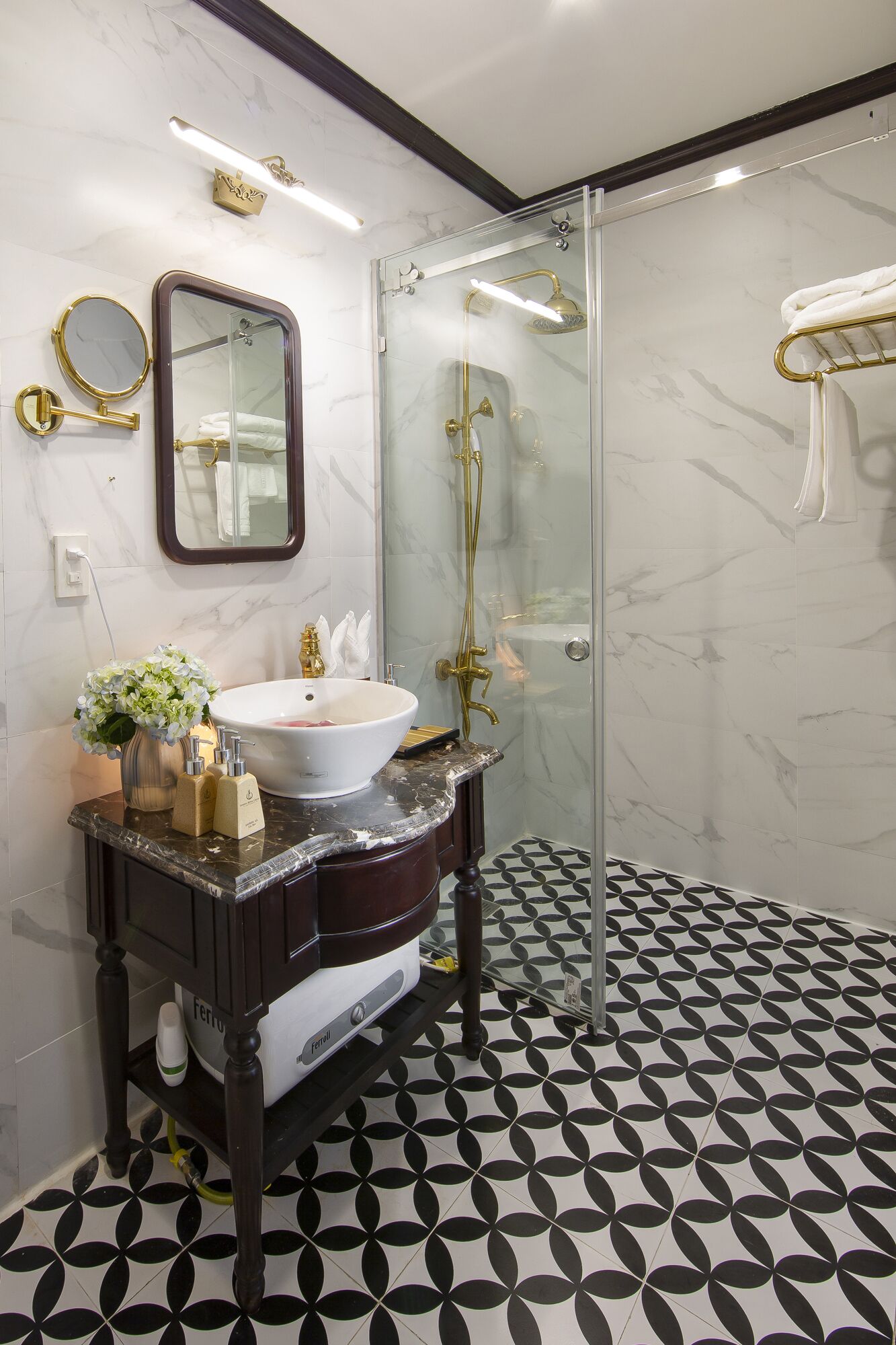 A modern bathroom with a glass-enclosed shower, a marble-tiled floor, and a vanity with a white sink and gold fixtures.