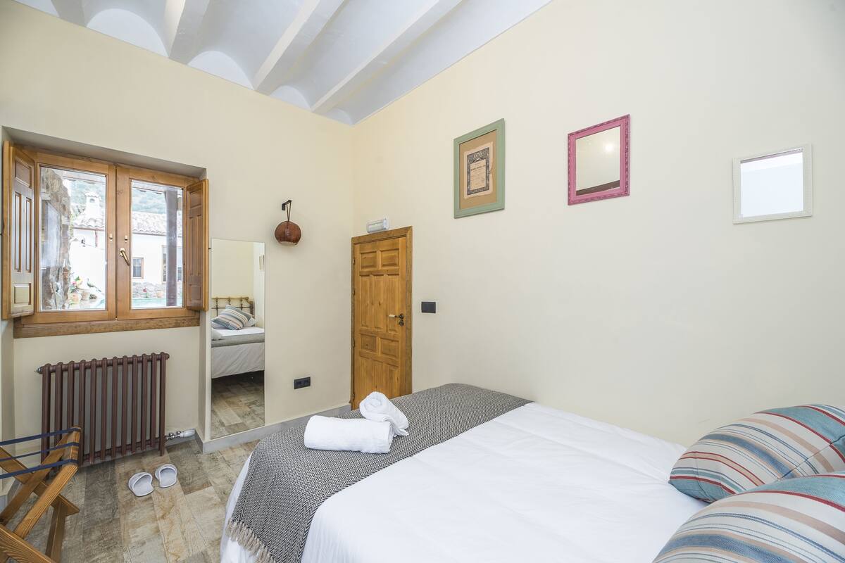 A bedroom with a bed, a wooden door, a radiator, and a window.