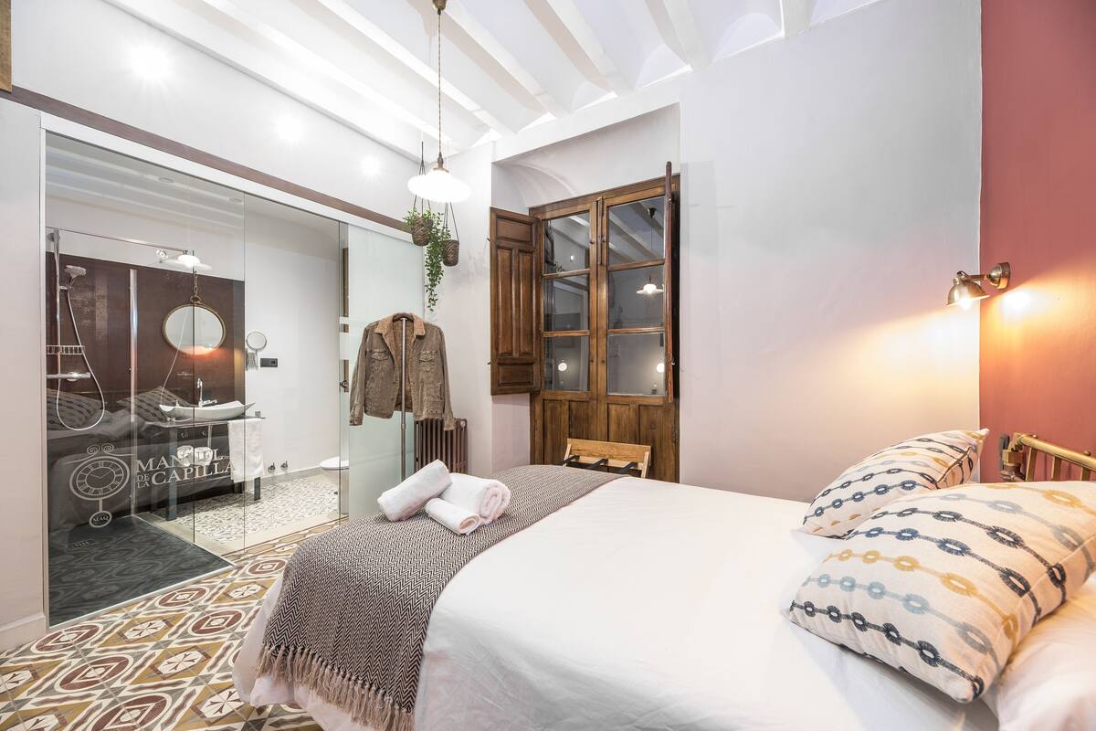 A bedroom with a bed, a wooden wardrobe, a mirror, and a window with curtains.