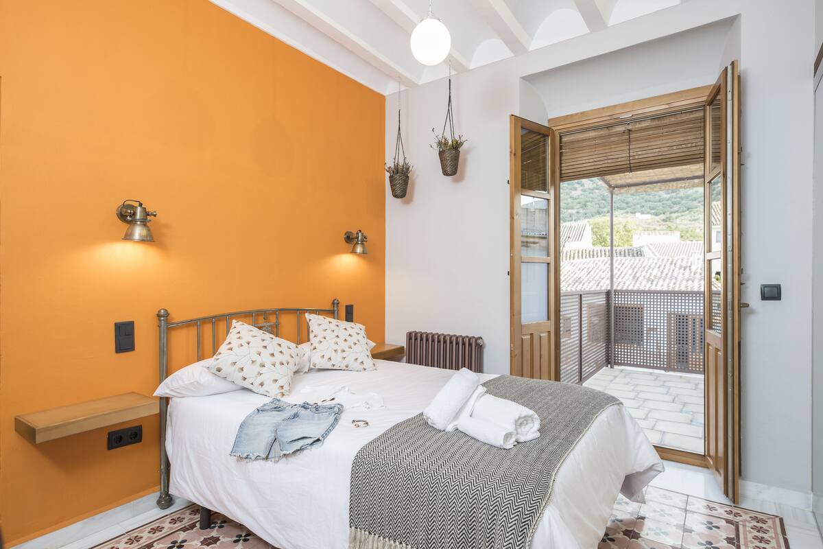 A bedroom with a bed, bedside table, and a view of the outside.