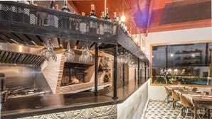 A restaurant with a brick oven, hanging light fixtures, and a view of the outdoors through a window. - Manuel de La Capilla (Cambil)