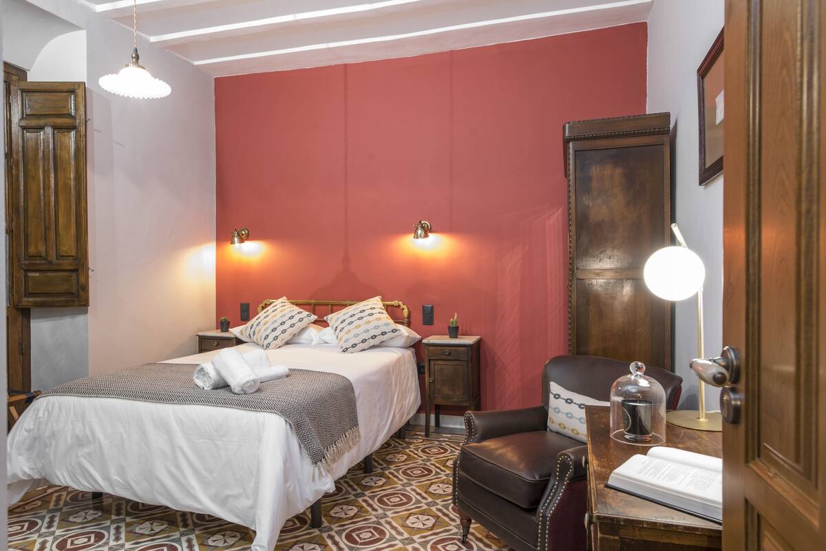 A bedroom with a bed, bedside tables, a chair, and a desk with a lamp.