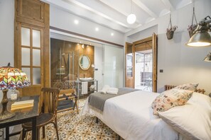 A hotel room with a bed, a desk with a lamp, a chair, a bathroom with a mirror, and a view of the outside. - Manuel de La Capilla (Cambil)