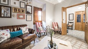 A cozy living room with a leather sofa, striped armchairs, and a coffee table with a vase and book. - Manuel de La Capilla (Cambil)