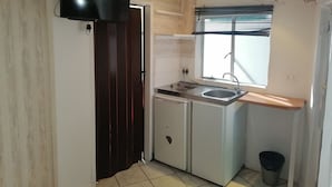 Une cuisine compacte équipée d’une cuisinière intégrée, d’un évier et d’une fenêtre avec des stores.