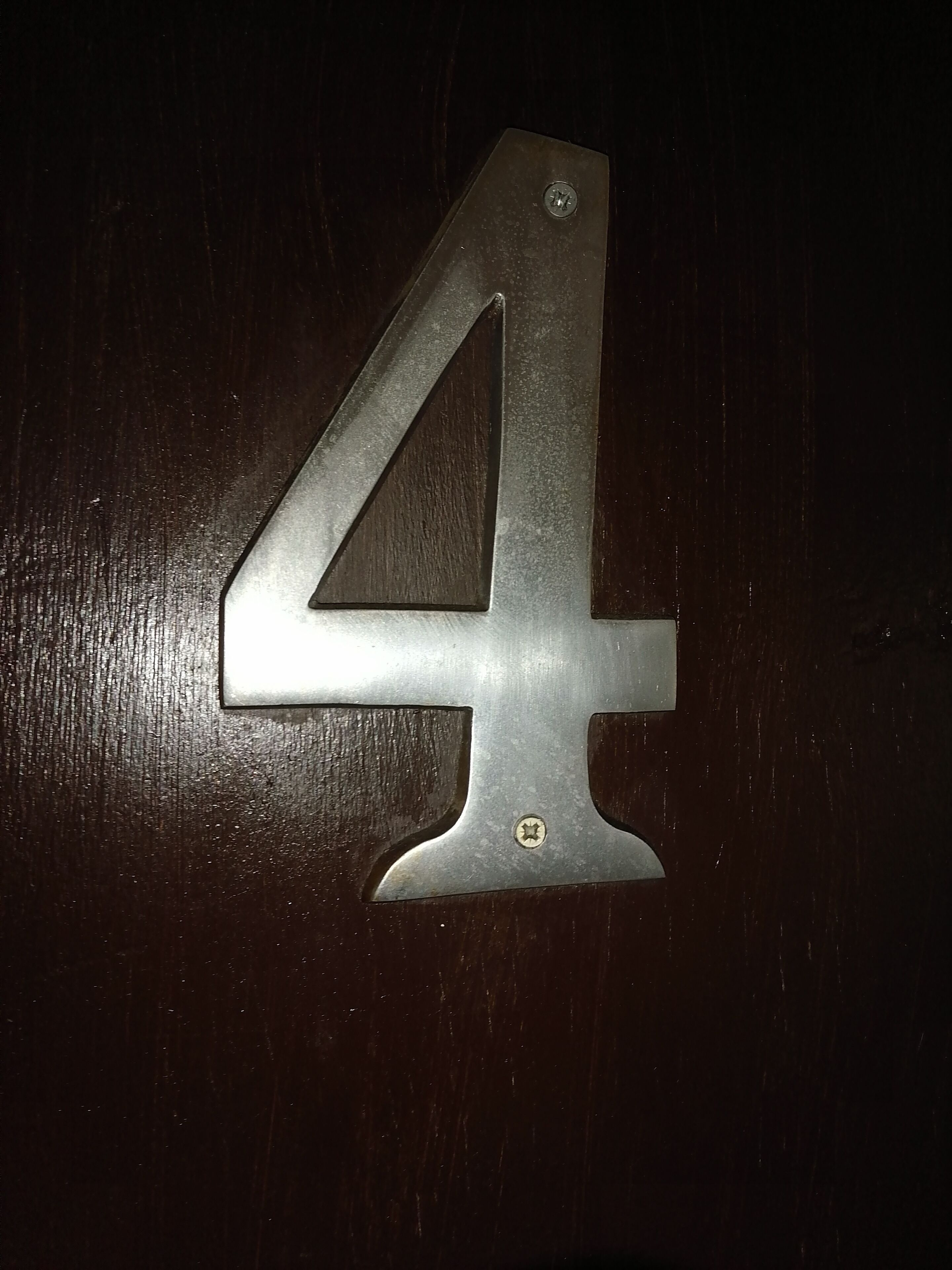 Un cartello in metallo con il numero 4 su una superficie di legno scuro.