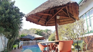 Un espace extérieur aménagé avec des sièges, un parasol en chaume, une piscine et une terrasse en briques.