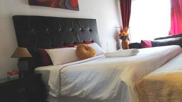 Una camera d'albergo con testiera trapuntata, un letto con lenzuola bianche, un cuscino rosso e bianco, una coperta gialla, una lampada e un quadro appeso al muro.