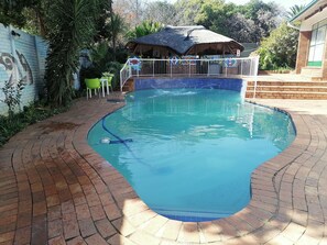Une piscine dont le bord est revêtu de carreaux, entourée d’une terrasse en briques et d’une clôture.