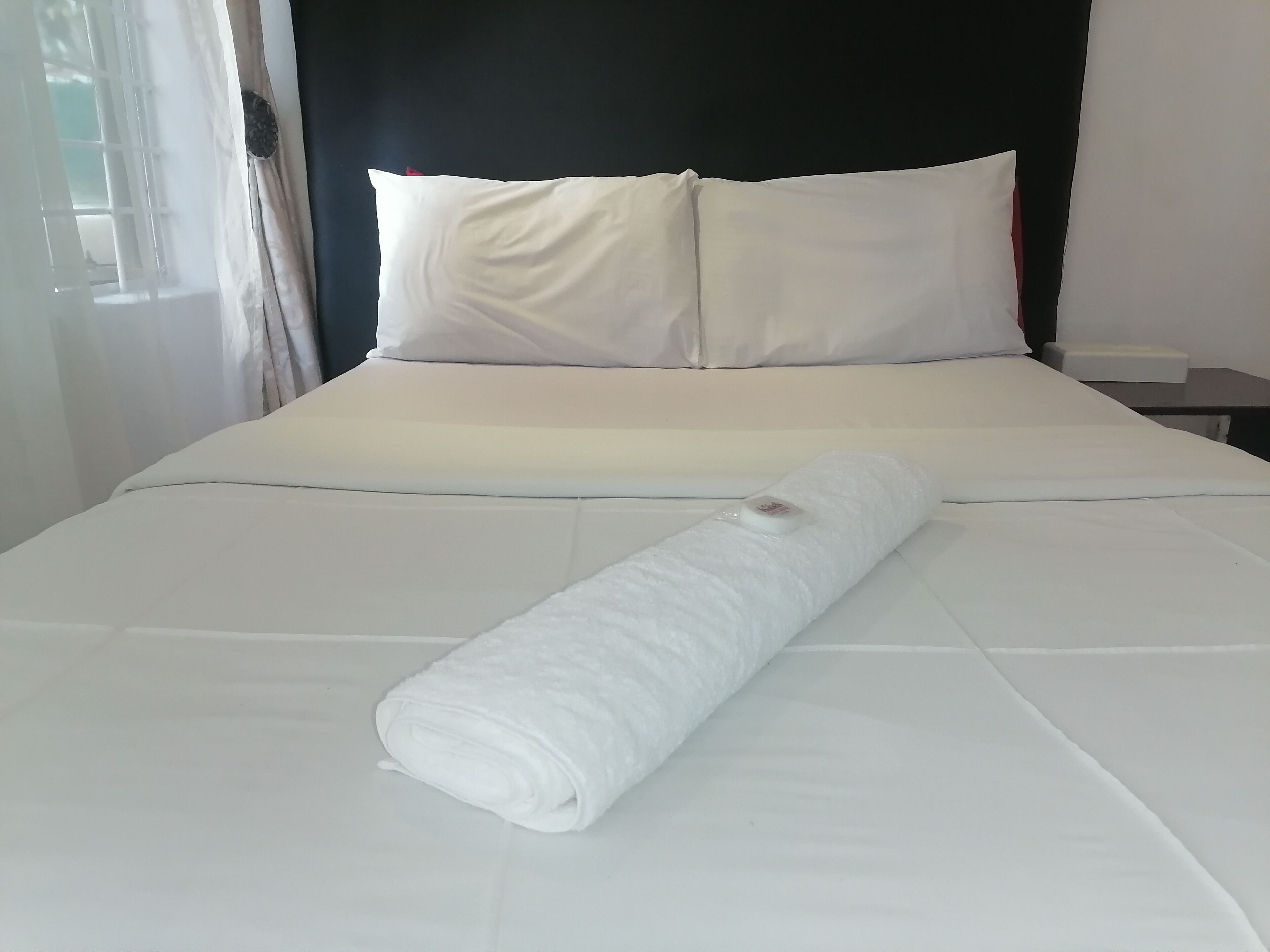 A neatly made bed with white linens and a rolled towel.