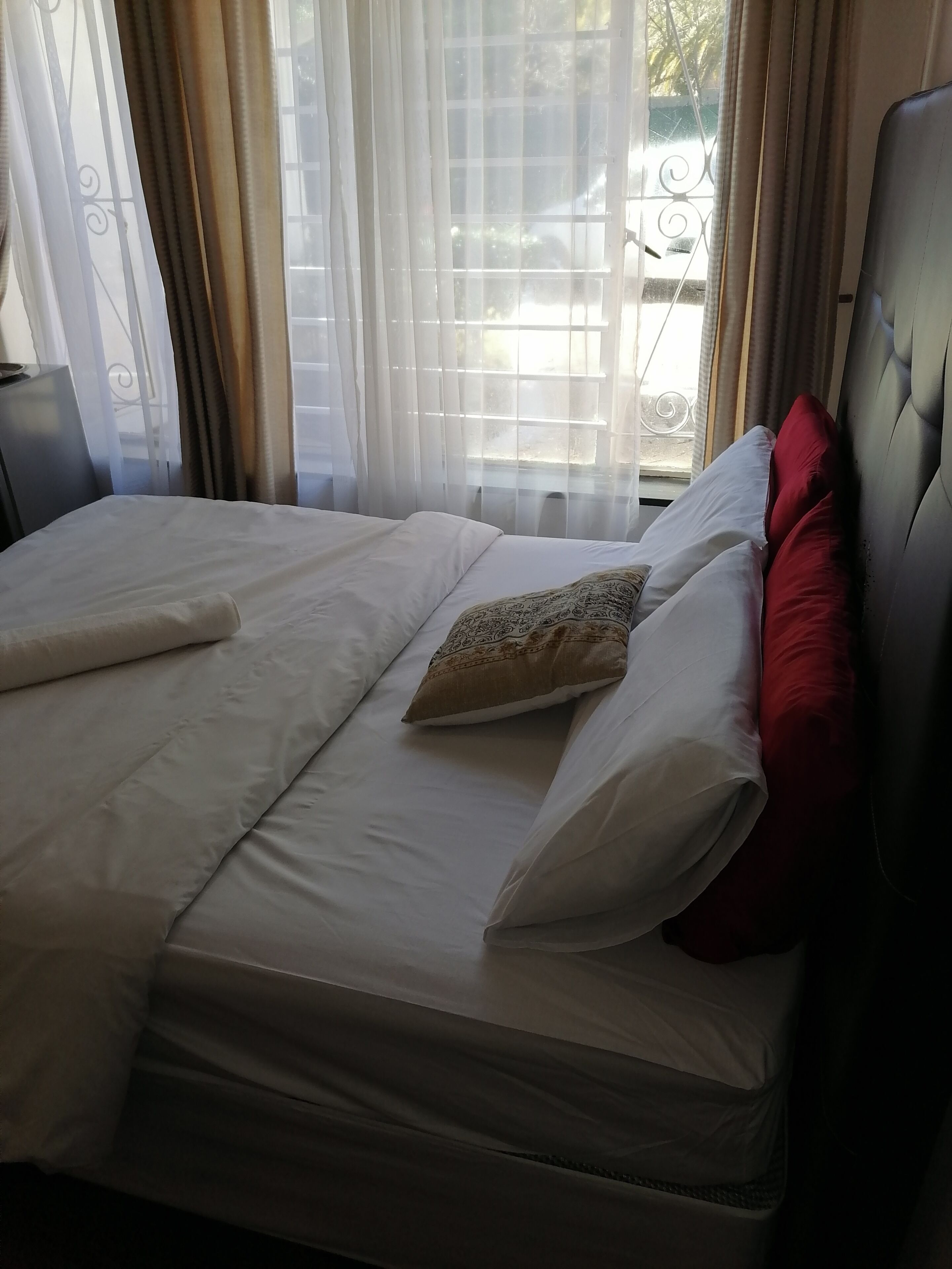A double bed with white bedding and a patterned pillow, a red pillow, and a black headboard.