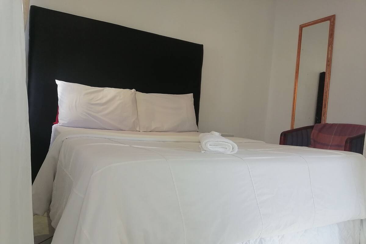 Un lit bien fait, avec des draps blancs, une tête de lit noire et une serviette pliée posée sur le lit.