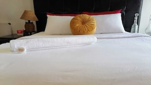 Un lit bien fait, avec du linge de lit blanc, une serviette enroulée et deux oreillers, dont l’un a un bord rouge et l’autre un motif jaune.