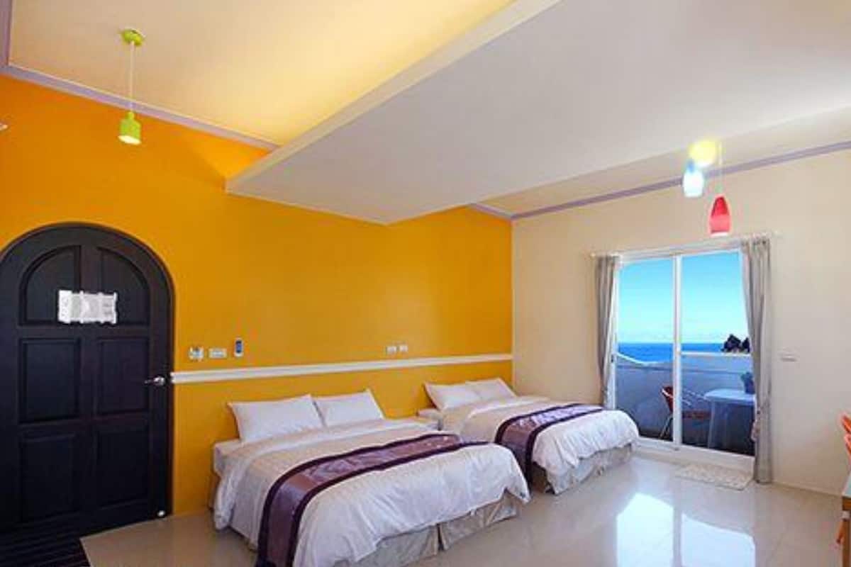 Une chambre d’hôtel avec deux lits, une porte, une fenêtre donnant sur un paysage agréable et un bureau.