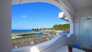 Uma varanda com vista para uma praia, uma linha costeira rochosa e um céu azul claro.