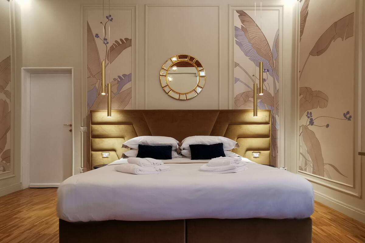 A large bed with a headboard, two bedside tables, and a mirror above it.