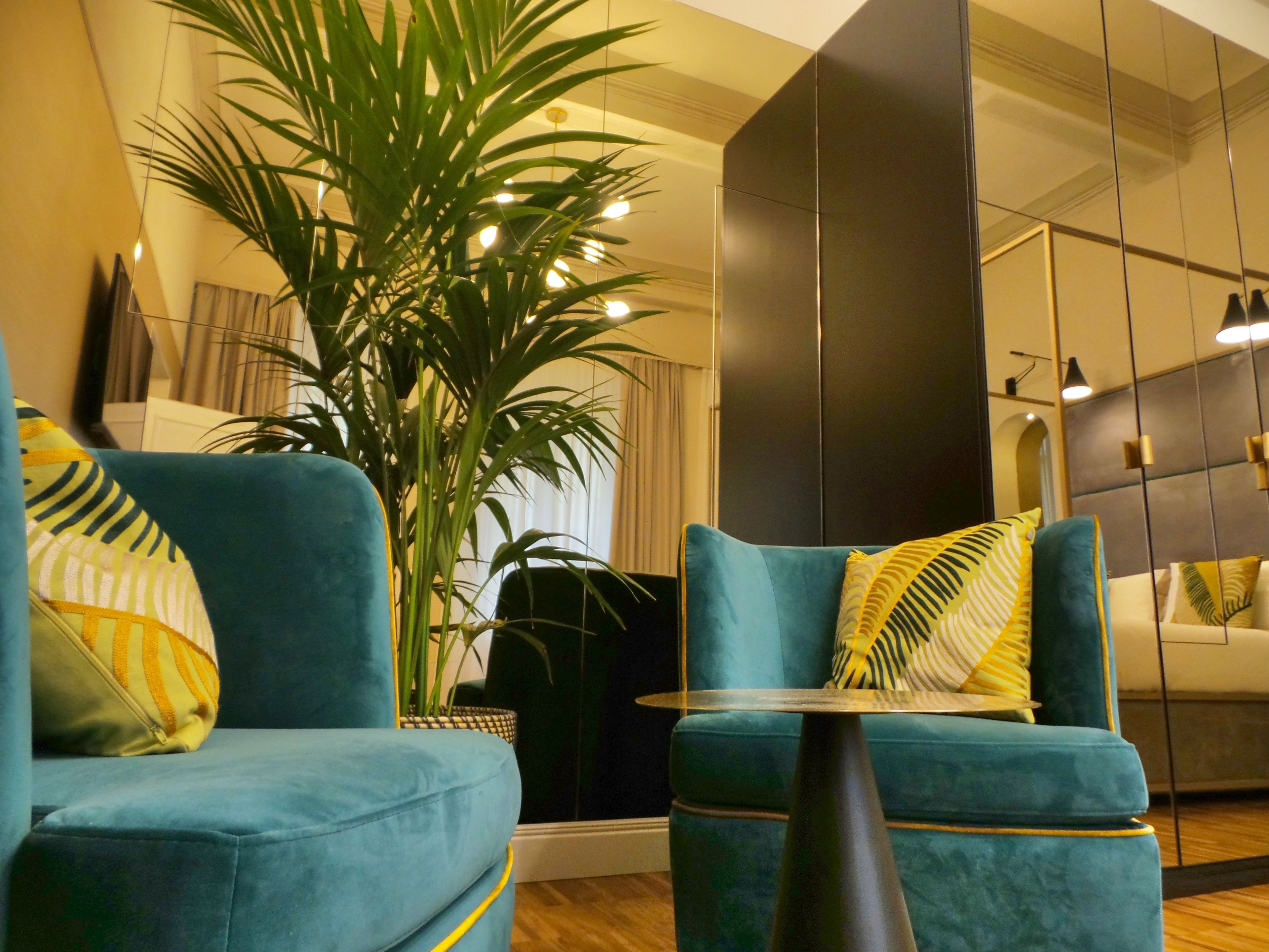 Un salon moderne avec des canapés de couleur turquoise, une grande plante en pot et un mur miroir.