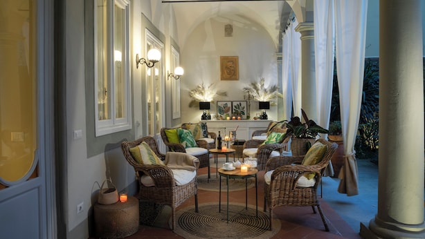 A cozy indoor seating area with wicker furniture, a central table with candles, and a view of the outdoors. - Ricasoli Garden Relais (Florence)