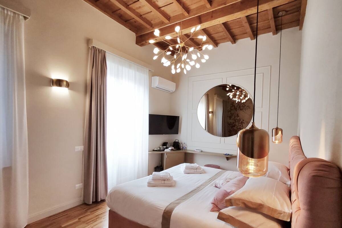 A hotel room with a wooden ceiling, a large bed with white bedding, a round mirror, and a TV on a desk.