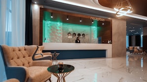 Un área de recepción moderna con piso de mármol, mostrador de recepción y zona de estar con un sillón tapizado y una mesita.