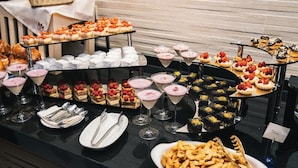 Un bufé con diversos postres y bebidas, como pasteles, repostería y tartaletas de frutas.