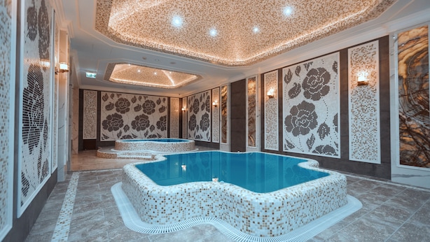 Un área de piscina interior lujosa con paredes de mosaicos y una piscina central.