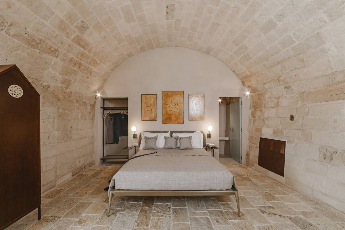 A bedroom with a stone arch ceiling, a large bed, bedside lamps, and a fireplace.