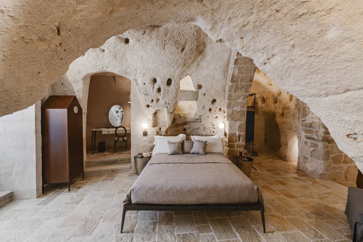 A bedroom with a stone ceiling, a bed, a nightstand, a wooden cabinet, and a stone wall.