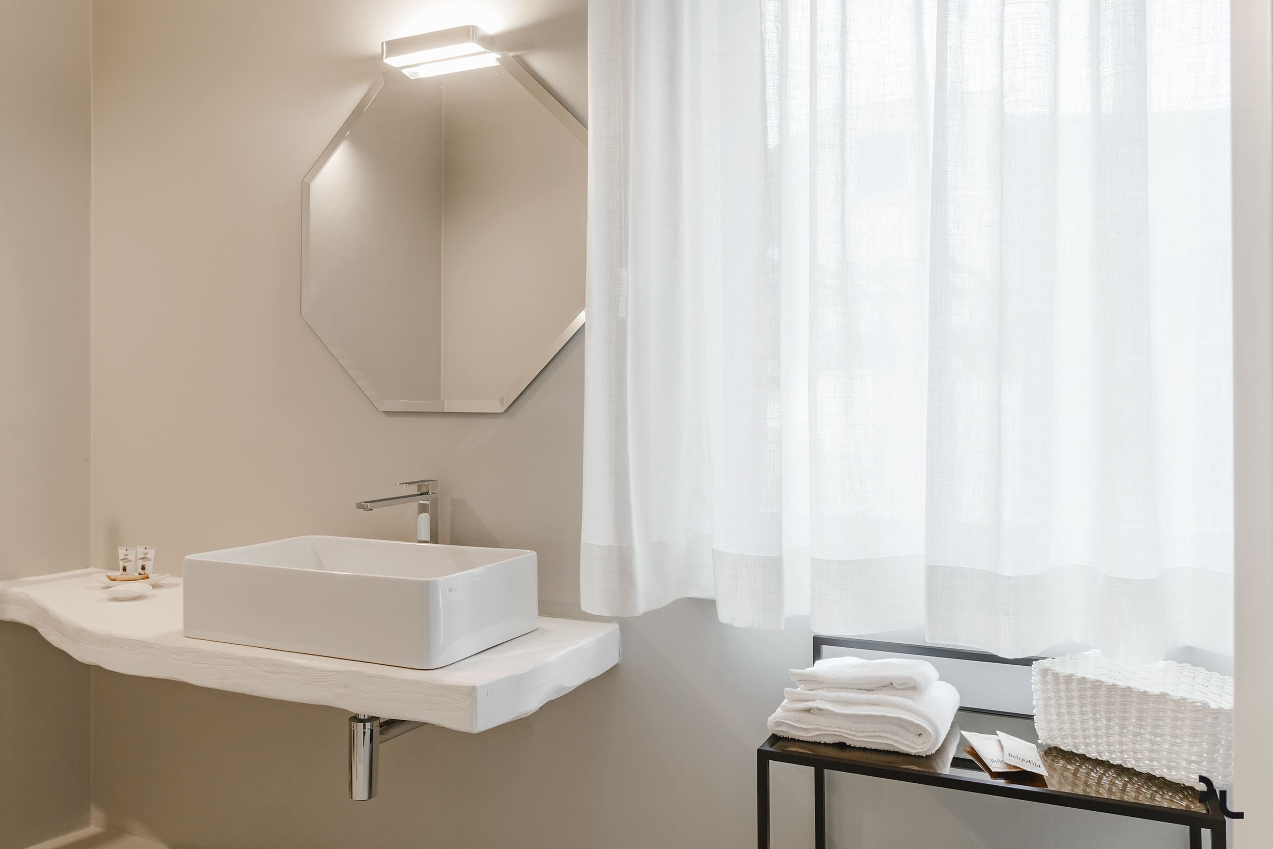 Een moderne badkamer met een witte wastafel, een grote spiegel en een raam met dunne gordijnen.