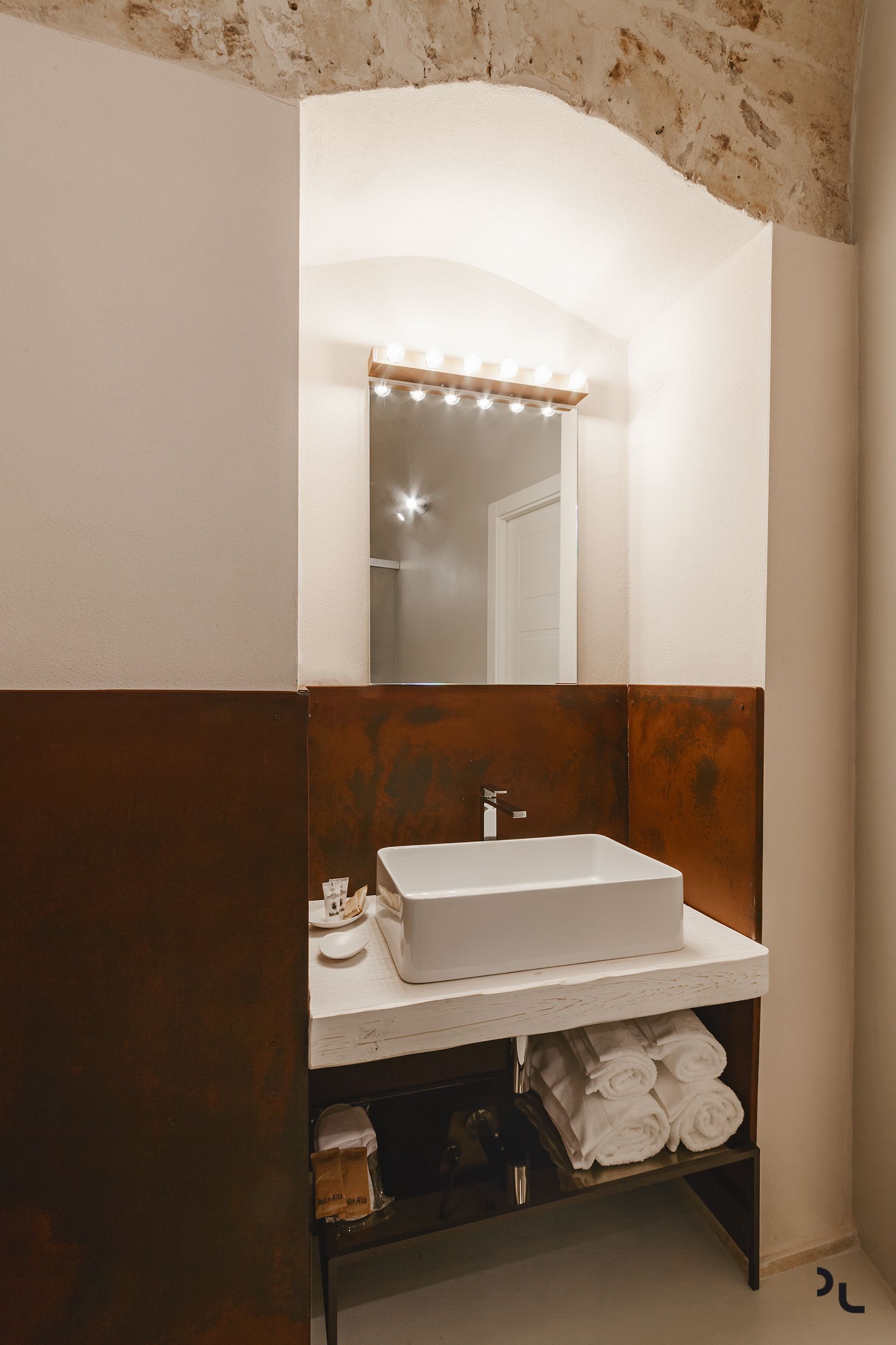 A bathroom with a white sink, a mirror with lights, and a towel rack.