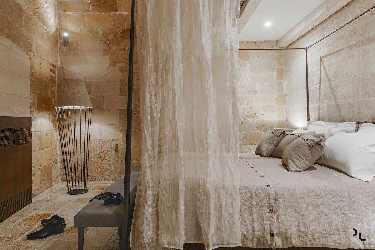 A bedroom with a bed, a bench, a lamp, and a wall with a textured pattern.