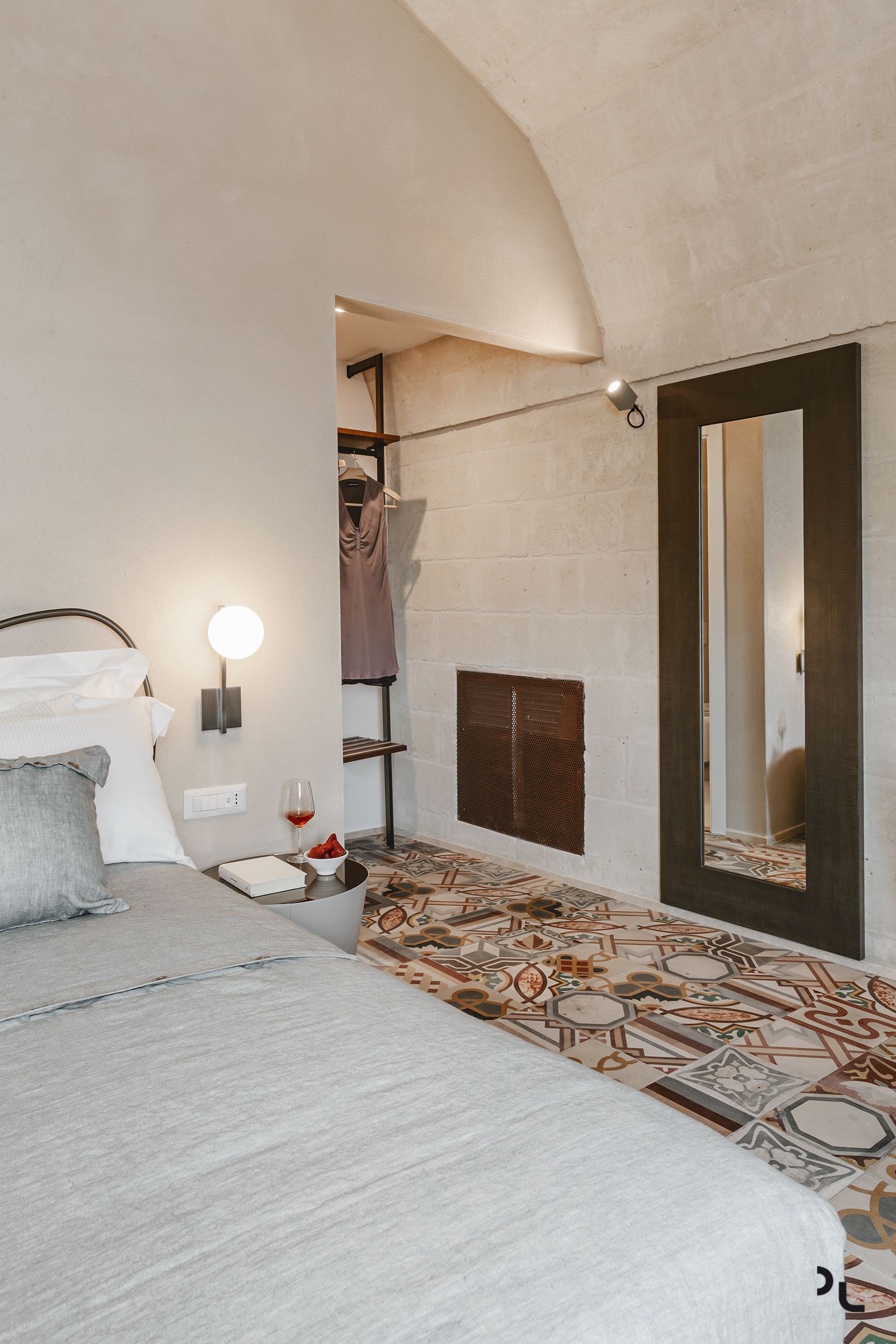 A bedroom with a bed, bedside table, lamp, and a patterned floor.
