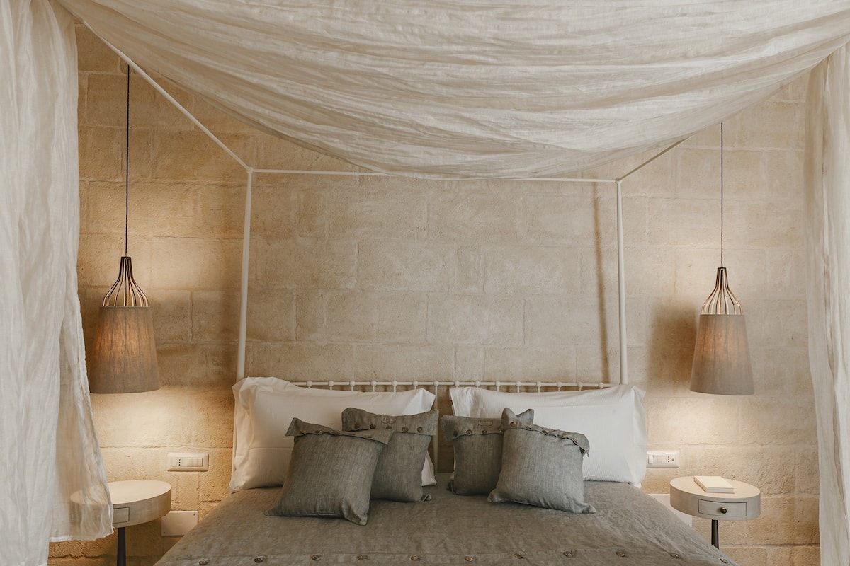 A bedroom with a stone wall, a canopy bed, and two bedside lamps.