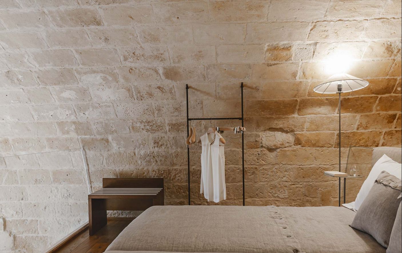 A bedroom with a stone wall, a bed, a bedside table, and a hanging light fixture.