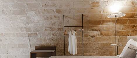 A bedroom with a stone wall, a bed, a bedside table, and a hanging light fixture.