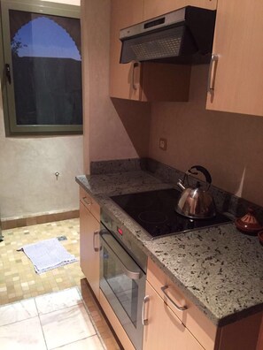 A compact kitchen with a stove, kettle, and granite countertop.
