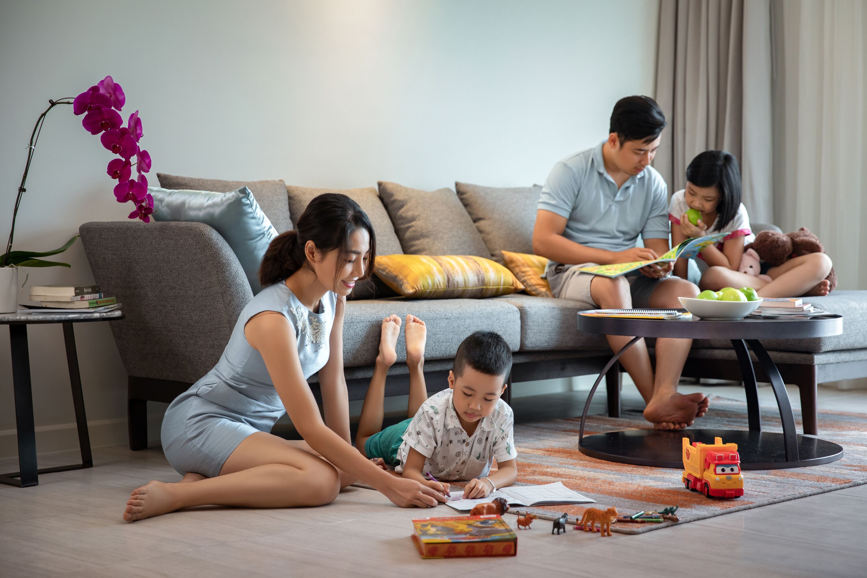 A family in a modern living room with a sofa, coffee table, and a small table with books and toys.