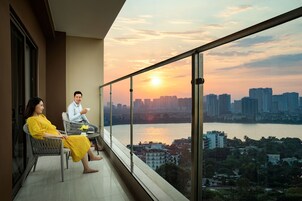 Balcón con vista a la ciudad al atardecer, dos personas sentadas y una mesa con una taza.