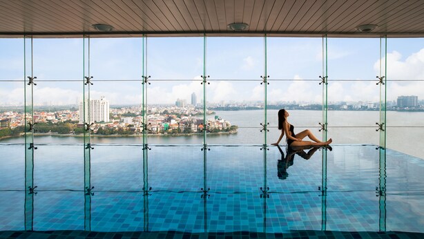 Une femme est assise au bord d’une piscine à débordement, avec une vue sur le paysage urbain.