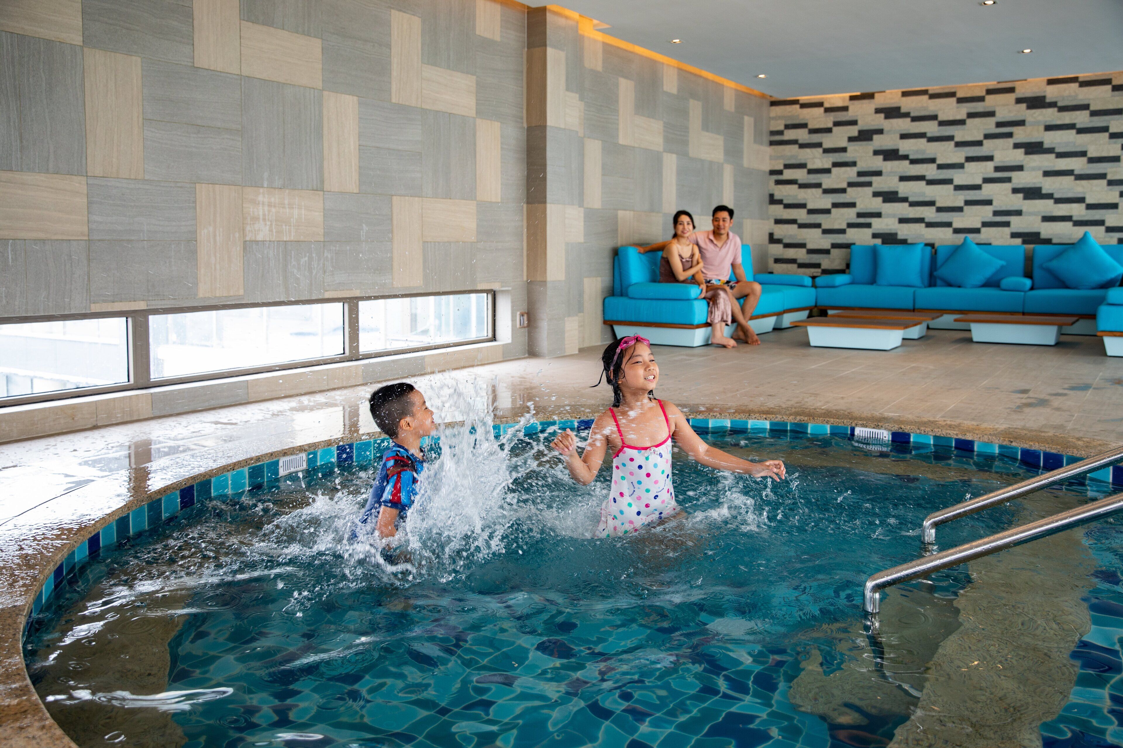 A swimming pool area with tiled walls, a blue sofa, and a poolside railing.