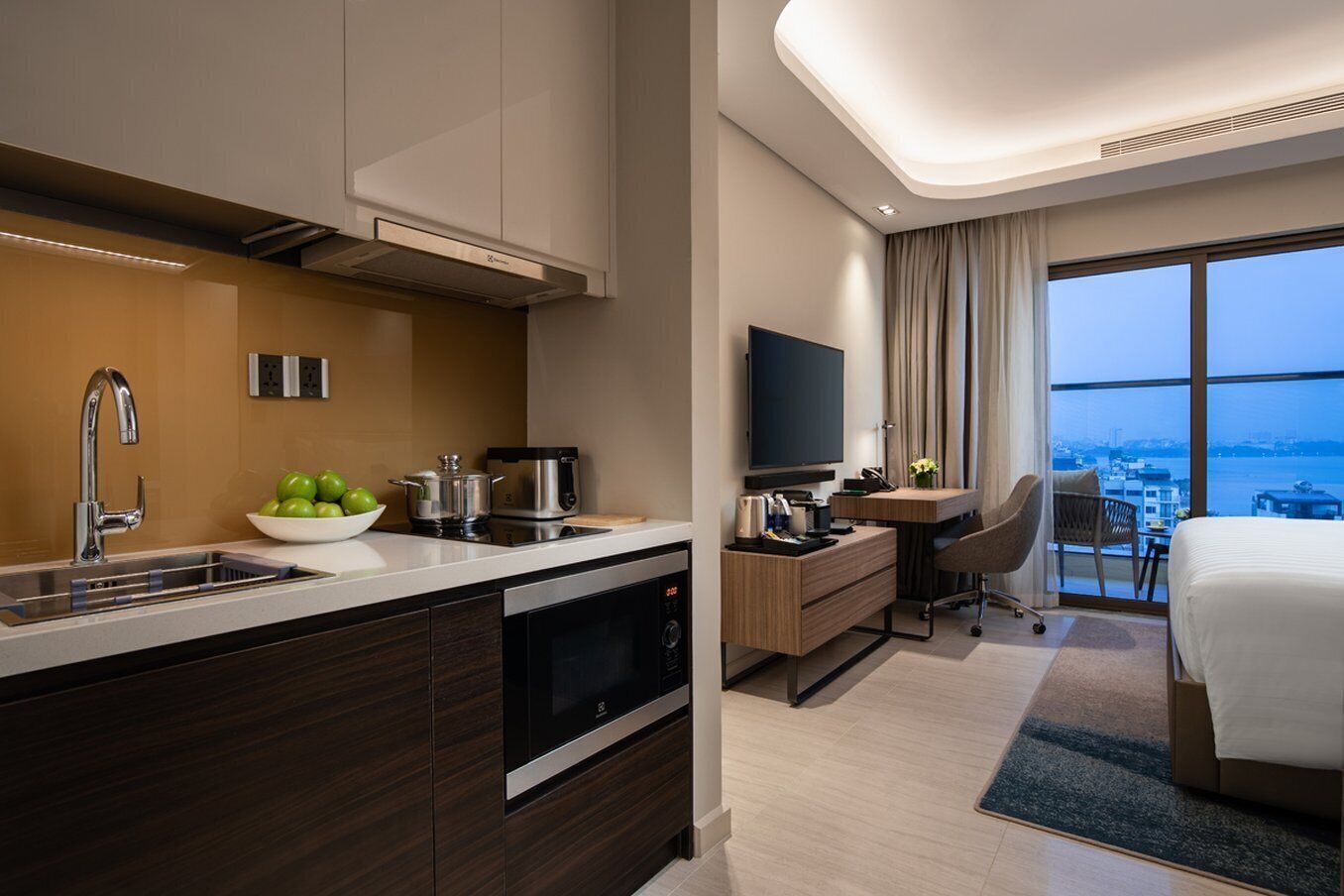 Een moderne hotelkamer met een keukenhoek, een groot bed, een bureau met stoel en een televisie.