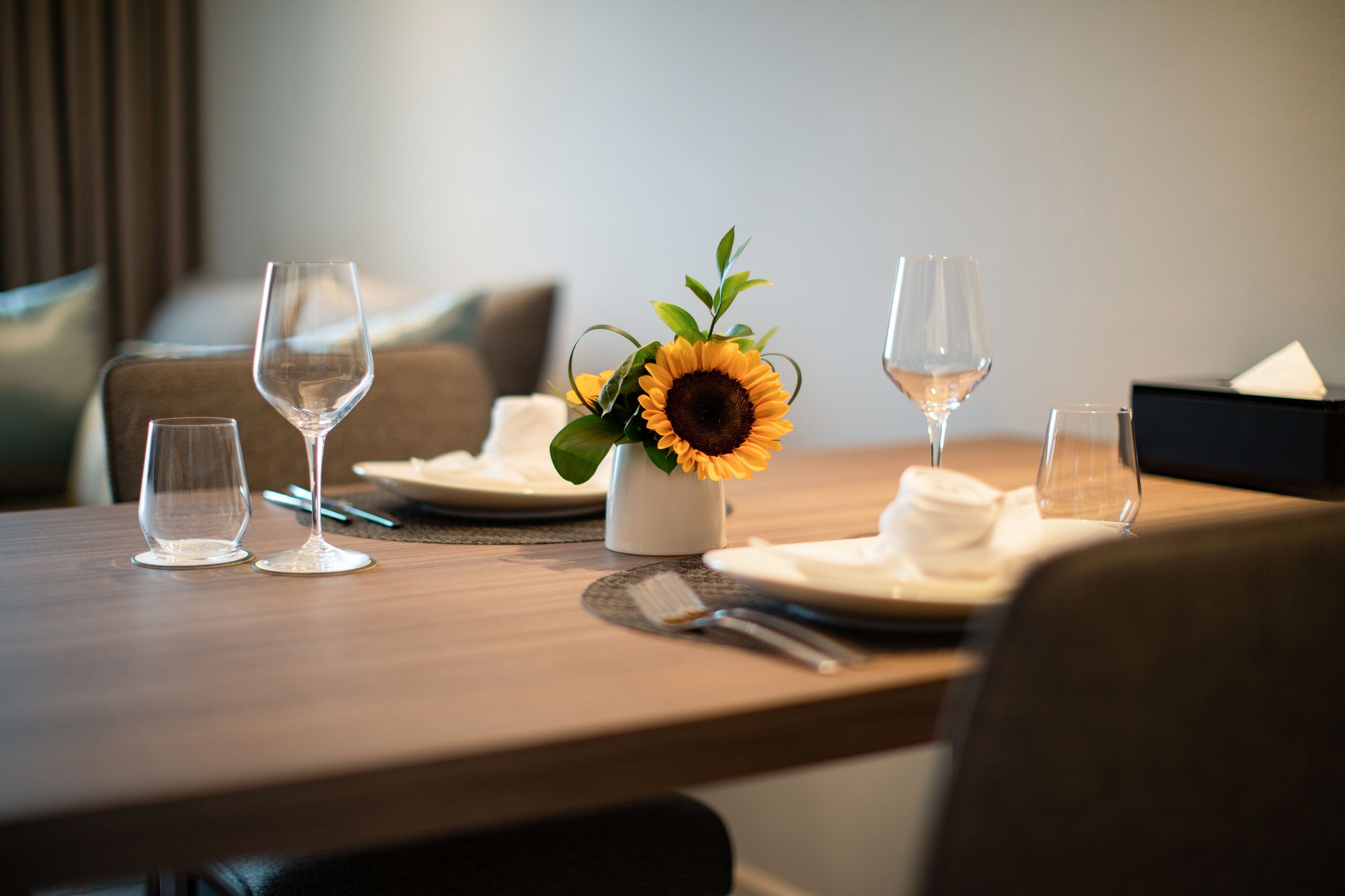 A dining table set with wine glasses, a vase with a sunflower, and a napkin holder.