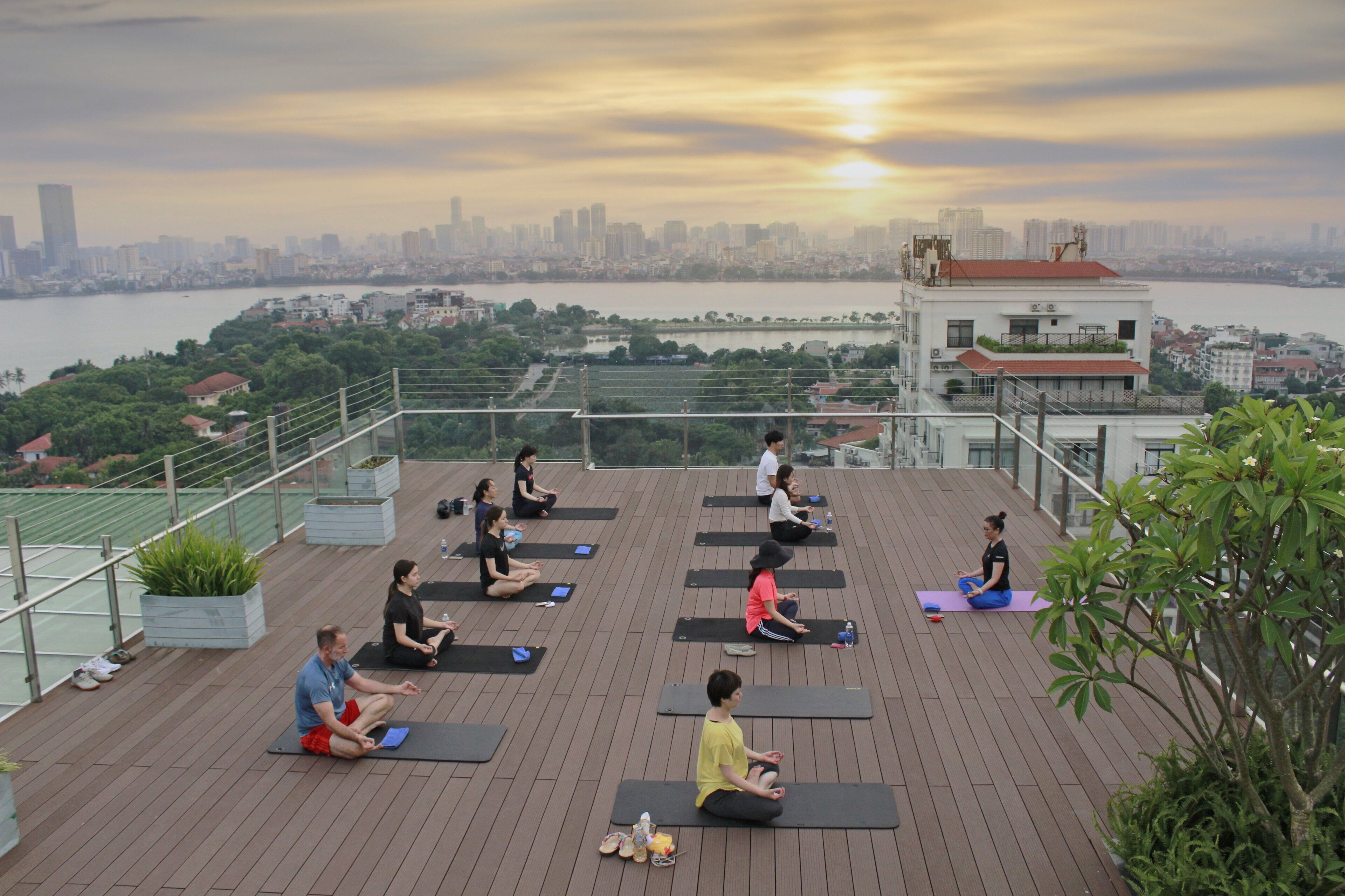 Un cours de yoga sur un toit, où les participants, sur leurs tapis, peuvent admirer un paysage urbain et une étendue d’eau.