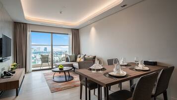 A modern hotel room with a dining area, a sofa, a TV, and a city view.